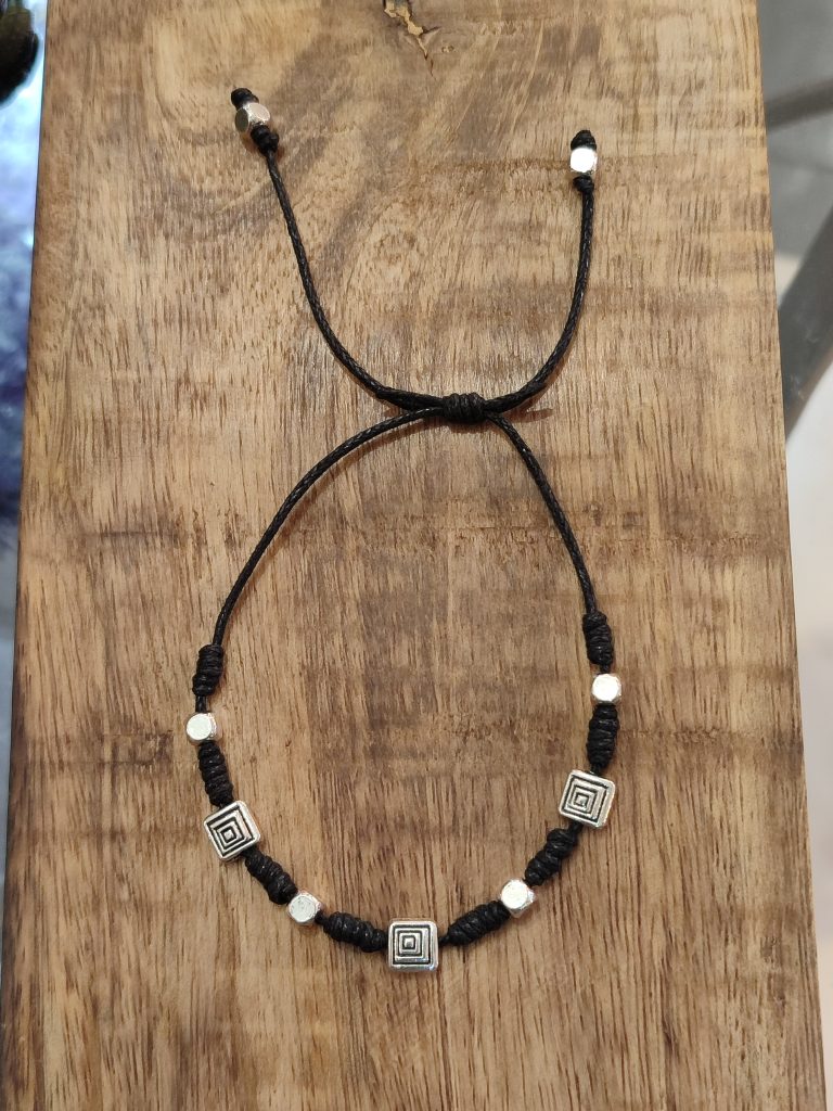 Pulsera amuleto de protección con cordón negro y símbolos geométricos de resguardo energético para bloquear vibraciones negativas.