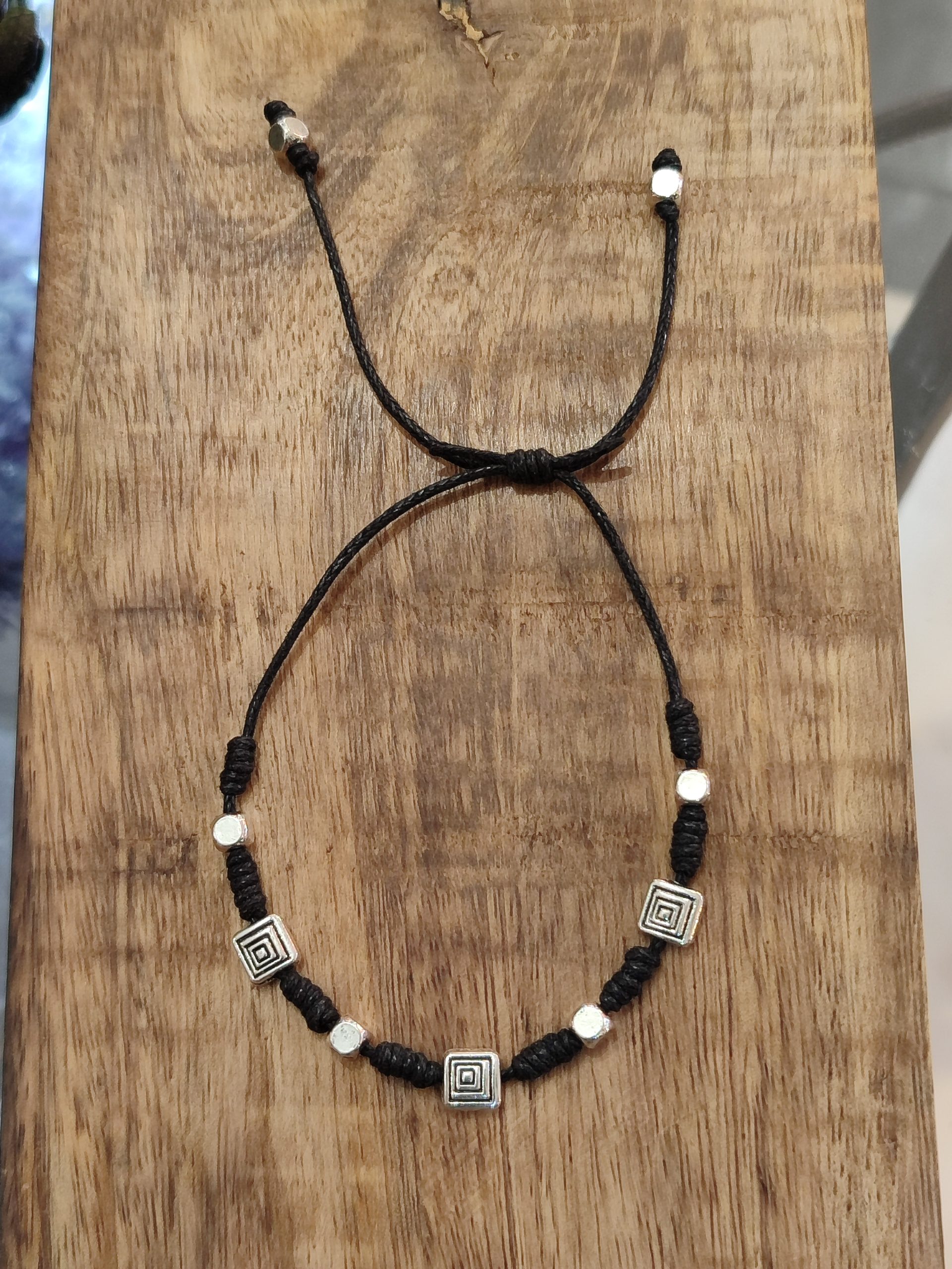 Pulsera amuleto de protección con cordón negro y símbolos geométricos de resguardo energético para bloquear vibraciones negativas.