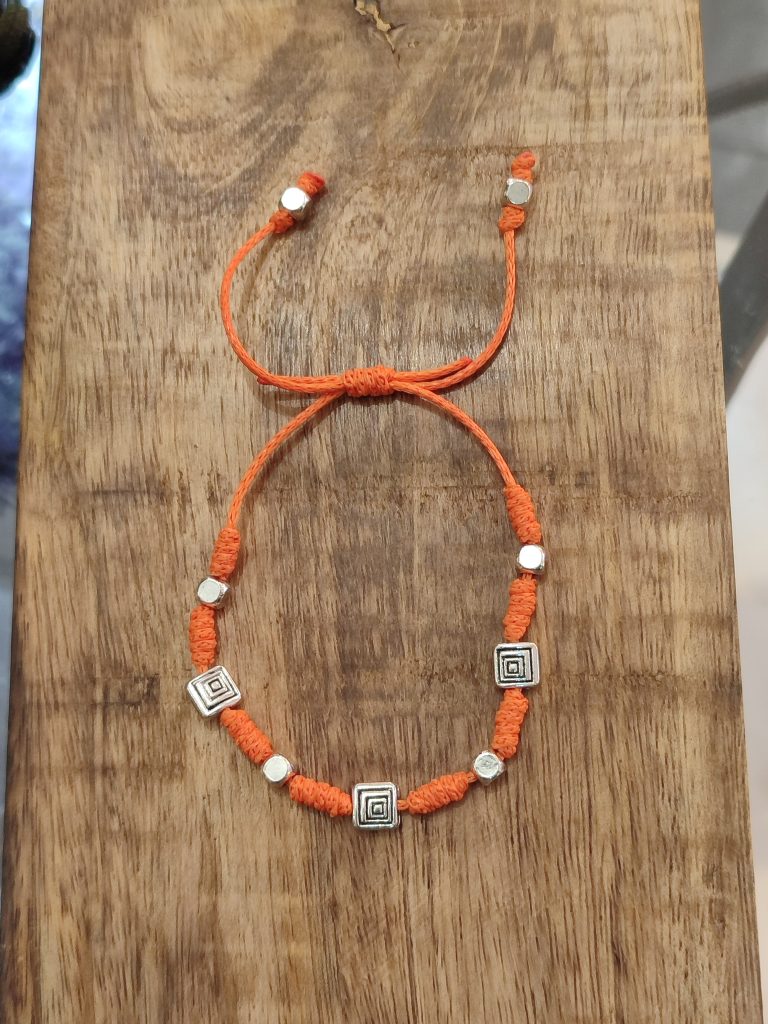 Pulsera amuleto para viajes y salud de cordón naranja con cuentas geométricas plateadas.