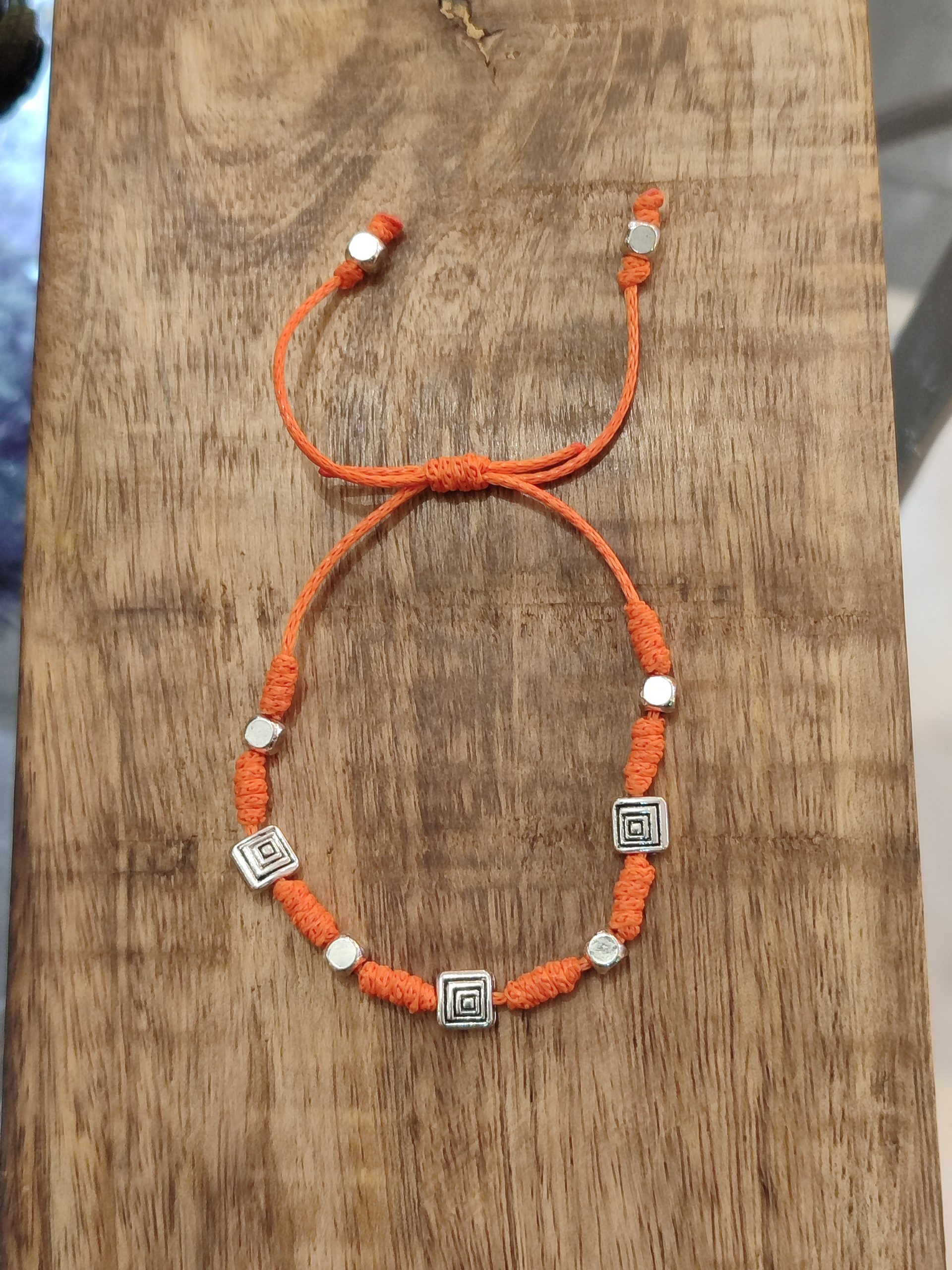 Pulsera amuleto para viajes y salud de cordón naranja con cuentas geométricas plateadas.
